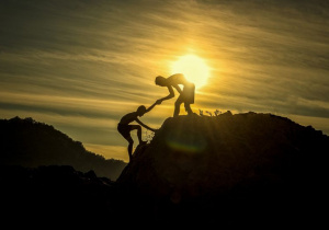 osoba pomaga drugiej osobie wspiąć się na górę