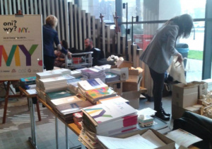Ludzie uczestniczący w konferencji oraz książki na wystawie.