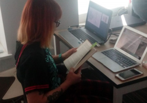 Rudowłosa dziewczyna- prowadząca spogląda na swoją prezentację w laptopie.